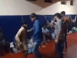 कैदी जमीन पर बैठकर बर्तनों को बजाते और नाचते दिखे